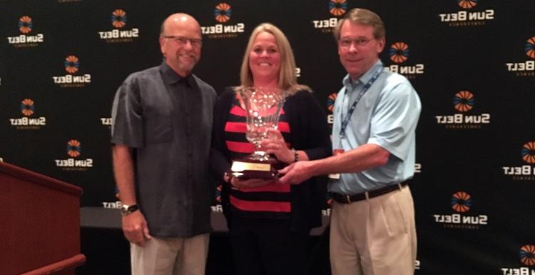 Dr. 约翰。史密斯, 左, USA executive vice president; Jinni Frisbey, USA associate athletic director of sports medicine and senior woman administrator; and Sun Belt Commissioner Karl Benson are pictured with the Bubas Cup, 连续第二年被授予南阿拉巴马州. 